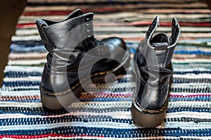 Back view of two robust, black ankle leather boots on a colorful rug as a concept of blisters