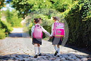 Back view of a two school girls wearing backpack outside the primary school. Kids after lessons going home. End of study