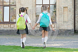 back view of two schoolgirls with school backpack walking together outdoor. childhood