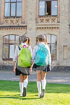 back view of two schoolkids with school backpack walking together outdoor