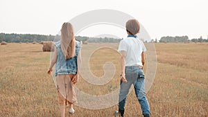 Back view of two stylish teens walking together in rural field