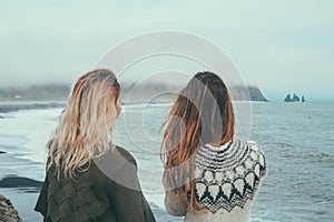 Back view of two woman standing on the shore of the sea and enjoying the landscape of black beach, troll toes in Iceland