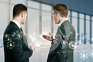 Back view of two young businessmen discussing contract on blurry office background with glowing polygonal network hologram.