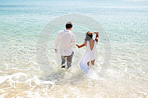 Back view of a two young just married couple enter in clothing in water, summer time, holiday in Greece. Honeymoon.