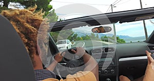 Back view of two young male friends driving in convertible on coastal highway