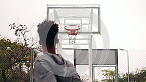 Back view of unrecognizable african player throwing ball in a basketball hoop, the ball hits the ring and scores