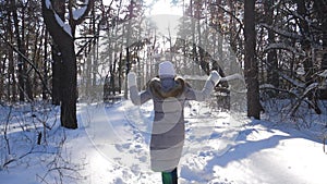 Back view of unrecognizable girl running on trail through snowy forest with sunlight at background. Happy woman enjoying