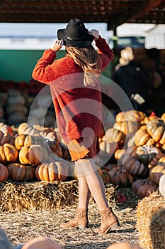 Back view of unrecognizable woman in brown cardigan and black hat on farmers market among stack of different orange