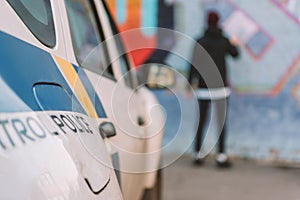 back view of vandal painting graffiti on wall, police car