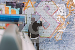 back view of vandal painting graffiti on wall, police car