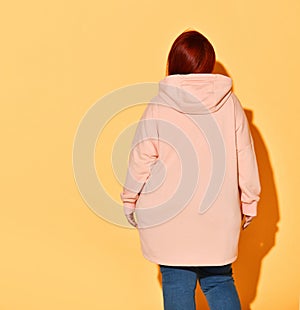 Back view of a voluptuous lady in jeans and bright yellow hoodie putting capuche on her head.
