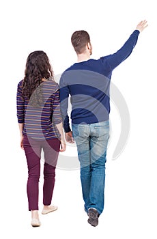 Back view of walking young couple (man and woman) pointing.