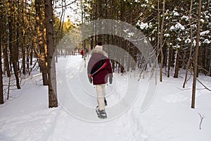 Back view of warmly dressed woman walking with snow shoes in path with couple in soft focus background