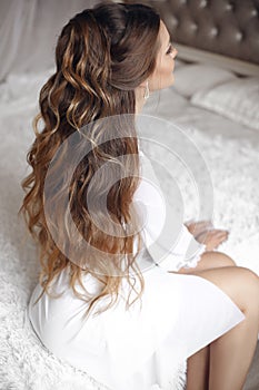Back view of wedding hairstyle. Beautiful brunette Bride Portrait with curly hair style wearing in white boudoir dressing go