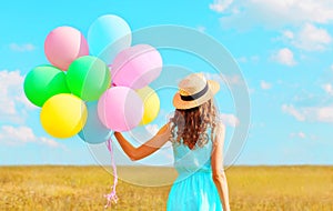 Back view woman with an air colorful balloons in a straw hat enjoying a summer day on a field and blue sky