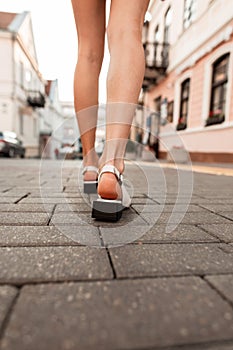 Back view of woman with beautiful legs in fashionable elegant shoes from the new summer collection. Girl walks on a stone road in