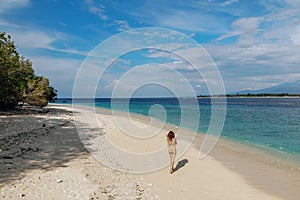 Back view of Woman in beige bikini walking on beach with turquoise ocean, blue sky. Gili Meno island, Bali, Indonesia. Tropical