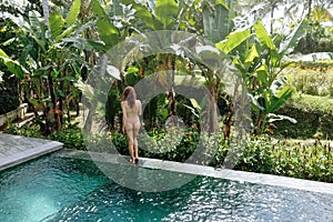 Back view of woman in bikini in a private pool in Bali admires a beautiful view of the palm trees.Luxury holiday.Girl