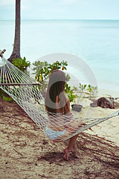 back view of woman in bikini resting in hammock with ocean