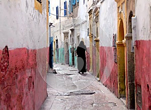 Back view of a woman in a black dress walking on a narrow street of Morocco