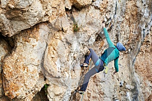 Back view woman climber resting and griping hold, climbs on a rocky wall