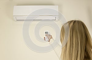 Back view of a woman controlling the air temperature in the house with a remote control. Home air conditioning concept.