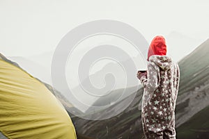 BAck view Woman dreamy in jumpsuit stand with mug of coffee wild camping outdoors enjoy carefree lifestyle think about life.