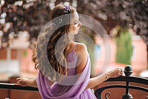 Back view of woman in evening dress stand on terrace and smile. Beautiful hairsyle