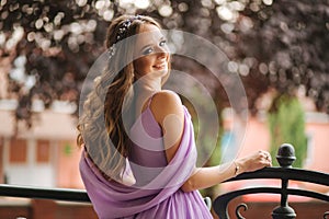 Back view of woman in evening dress stand on terrace and smile. Beautiful hairsyle