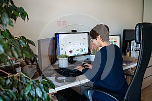 Back view woman in glasses typing on pc with headsets, few monitors on her work desk at home working space. Remote work concept.