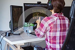 Back View Woman in a headset with Xbox controller playing video games on her desktop pc. Online time, virtual life photo