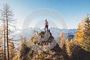 Back view of woman hiker with backpack standing on a rock admiring the view of autumn mountains