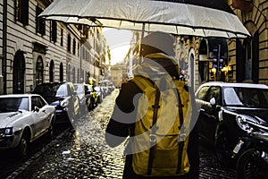 Back view of a woman holding an umbrella under the rain and walking down the street in Roma, Italy