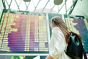 Back view of woman in international airport looking at the flight information board checking for flight