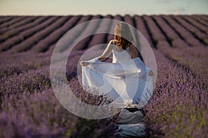 Back view woman lavender sunset. Happy woman in white dress holds lavender bouquet. Aromatherapy concept, lavender oil