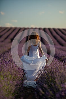 Back view woman lavender sunset. Happy woman in white dress holds lavender bouquet. Aromatherapy concept, lavender oil