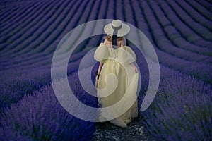 Back view woman lavender sunset. Happy woman in yellow dress holds lavender bouquet. Aromatherapy concept, lavender oil