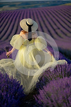 Back view woman lavender sunset. Happy woman in yellow dress holds lavender bouquet. Aromatherapy concept, lavender oil