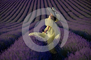 Back view woman lavender sunset. Happy woman in yellow dress holds lavender bouquet. Aromatherapy concept, lavender oil