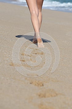 Back view of a woman legs walking on the beach and her traces