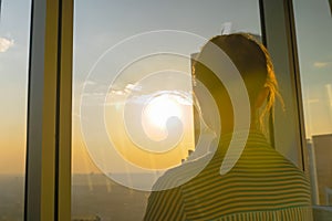 Back view of woman looking at cityscape through glass window of skyscraper