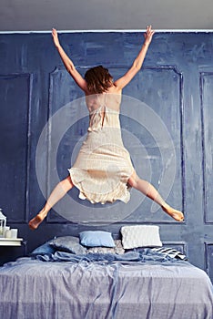 Back view of a woman in nightgown jumping on bed with arms and l