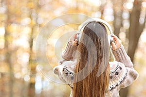 Back view of woman putting headphones in autumn