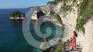 Back view of woman in red dress goes down and up the stairs cut down in a rock at the Diamond Beach, Nusa Penida island
