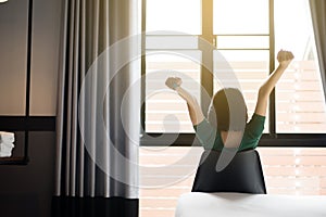 Back view of woman relaxing and sitting on chair with hands raise up and looking on window at house in the morning