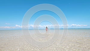 Back view of a woman running in water on sand in a beautiful island sandbar.