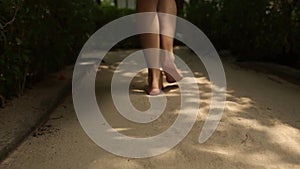 Back view of woman`s feet going to spa room bungalow on exotical tropical island. Smiling blonde girl walks barefoot on
