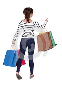 Back view of woman with shopping bags pointing .