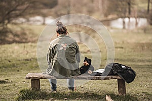 Back view of a woman sitting on a benc with a toy and a book next to her in the park