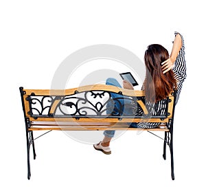 Back view of woman sitting on bench and looks at the screen the tablet.